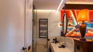 Un baño moderno con suelo de mármol, tocador con espejo, mesita de madera y pared de acento roja.