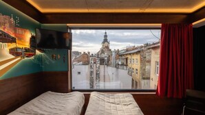 Una habitación con dos camas, un ventanal con vistas a la ciudad, un televisor de pantalla plana y una cortina roja.