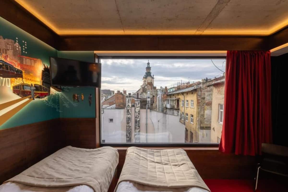 Une chambre avec deux lits, une grande fenêtre donnant sur le paysage urbain, un téléviseur à écran plat et un rideau rouge.