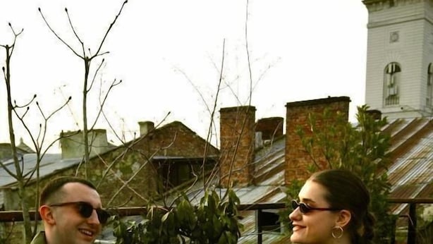 Dos personas cenando al aire libre con pizza y bebidas.
