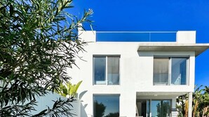 Un bâtiment moderne à deux étages, doté d’une piscine, d’un espace extérieur aménagé et surplombant un ciel d’un bleu limpide.