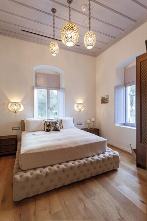 A bedroom with a large bed, two bedside tables, a window with shutters, and hanging light fixtures. - Aylin Executive Suites - Saray Suite (Rhodes)