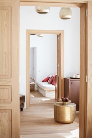 A wooden-framed doorway leading to a bedroom with a bed, a bedside table, and a small cabinet. - Aylin Executive Suites - Saray Suite (Rhodes)