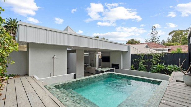 A modern outdoor pool area with a wooden deck, a covered seating area, and a small building structure. - Coastal Noir - Modern Cottesloe Stay (Cottesloe)
