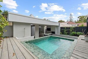 A modern outdoor pool area with a wooden deck, a covered seating area, and a small building structure. - Coastal Noir - Modern Cottesloe Stay (Cottesloe)