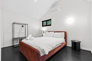A modern bedroom with a large bed, a side table, a small round table, and a wall-mounted air conditioner. - Coastal Noir - Modern Cottesloe Stay (Cottesloe)