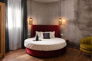 Ein rundes Bett mit rotem Kopfteil, zwei Wandleuchten, ein Nachttisch und ein gelber Sessel.