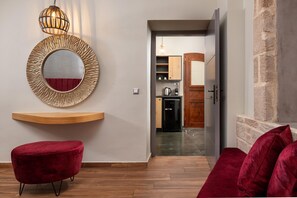Ein modernes Interieur mit einem roten Samottosche, einem runden Spiegel mit strukturierter Rahmung und einem Holzregal.