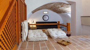 A bedroom with a wooden ceiling, a bed with white bedding, a clock on the wall, and a wine glass on the floor. - Belvedere Medieval Villa in Old Town (Old Town Rhodes)