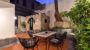 An outdoor patio with a table and chairs, surrounded by stone walls and greenery. - Belvedere Medieval Villa in Old Town (Old Town Rhodes)