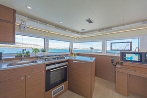 A modern kitchen with a large window, a stove, an oven, and a digital screen. - Sun-Kissed Sailing Adventure in Islas Sarónicas (Alimos)