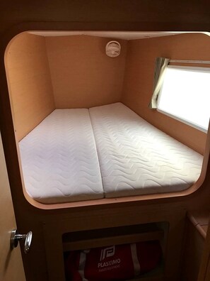 A compact, single-bed RV interior with a window on one side, a door with a handle, and a lower compartment labeled 'PLASTIMO SAFETY EQUIPMENT.' - Sun-Kissed Sailing Adventure in Isla de Mahe, Seychelles (Providence)