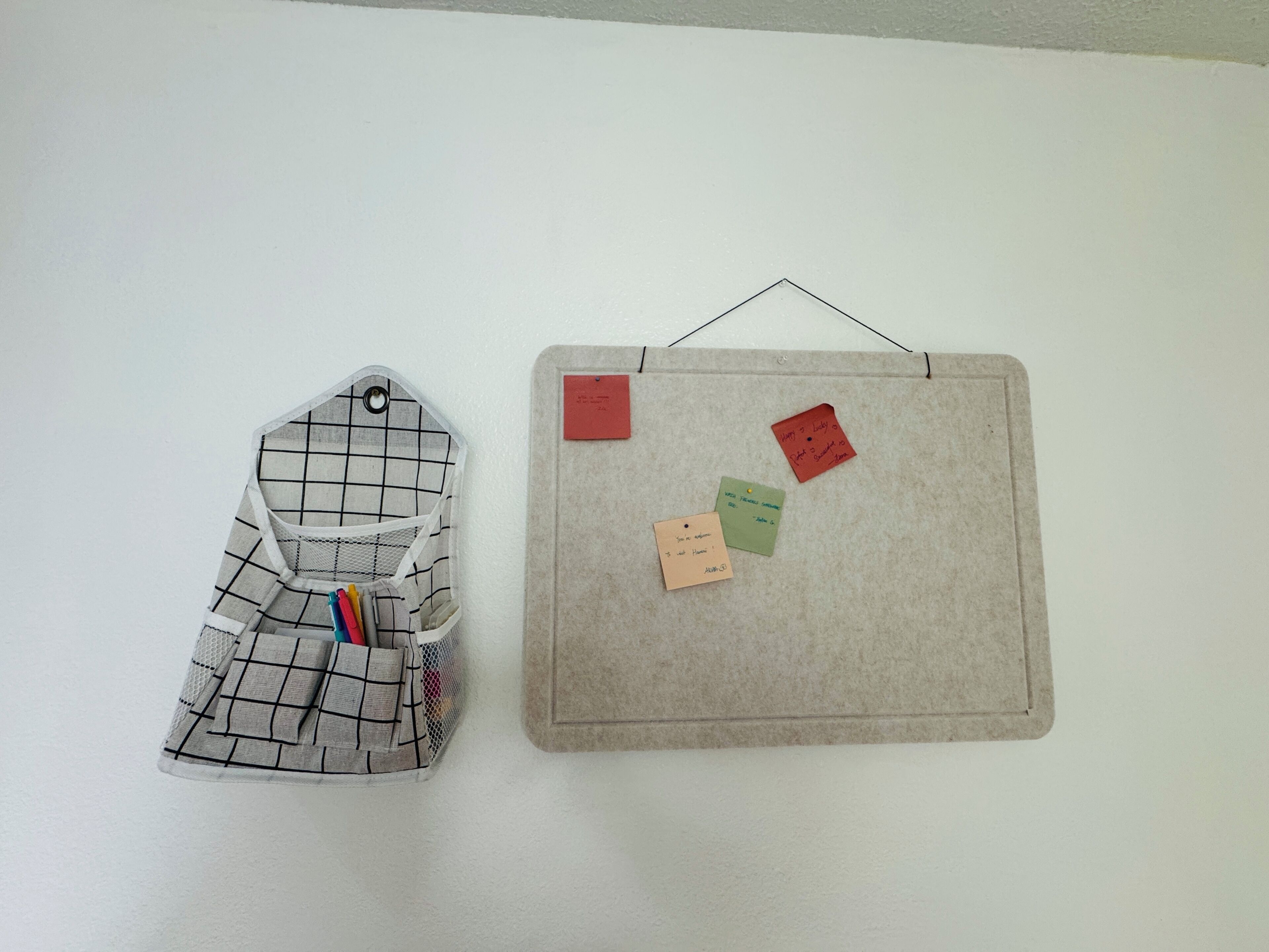 A wall-mounted bulletin board with four sticky notes and a fabric bag with a grid pattern.
