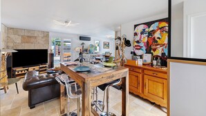 A modern living room with a large flat-screen TV, a wooden dining table, and a colorful abstract painting.