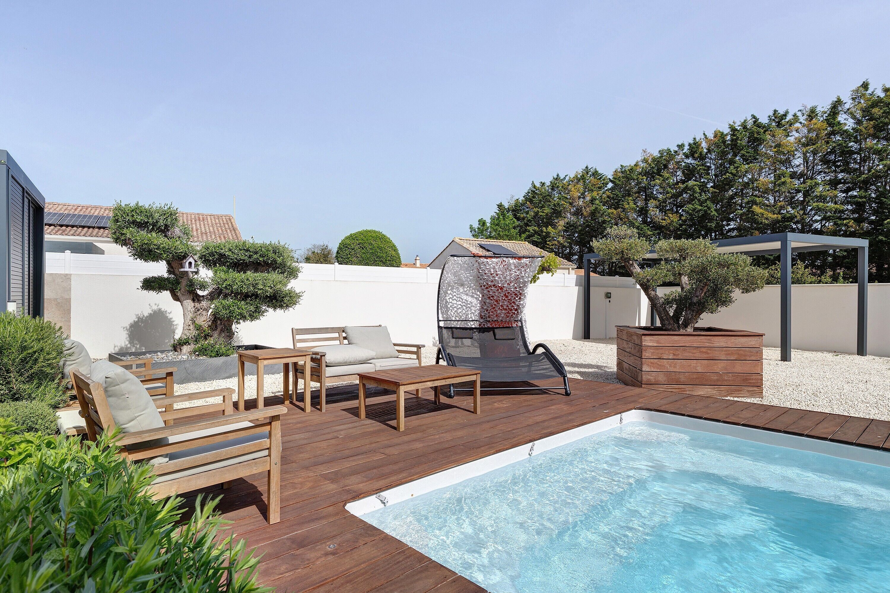 Un jardin avec une piscine, une terrasse en bois, des chaises longues et un espace barbecue.
