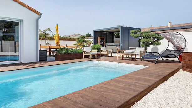 A modern outdoor pool area with wooden decking, lounge chairs, and a small structure with a roof.