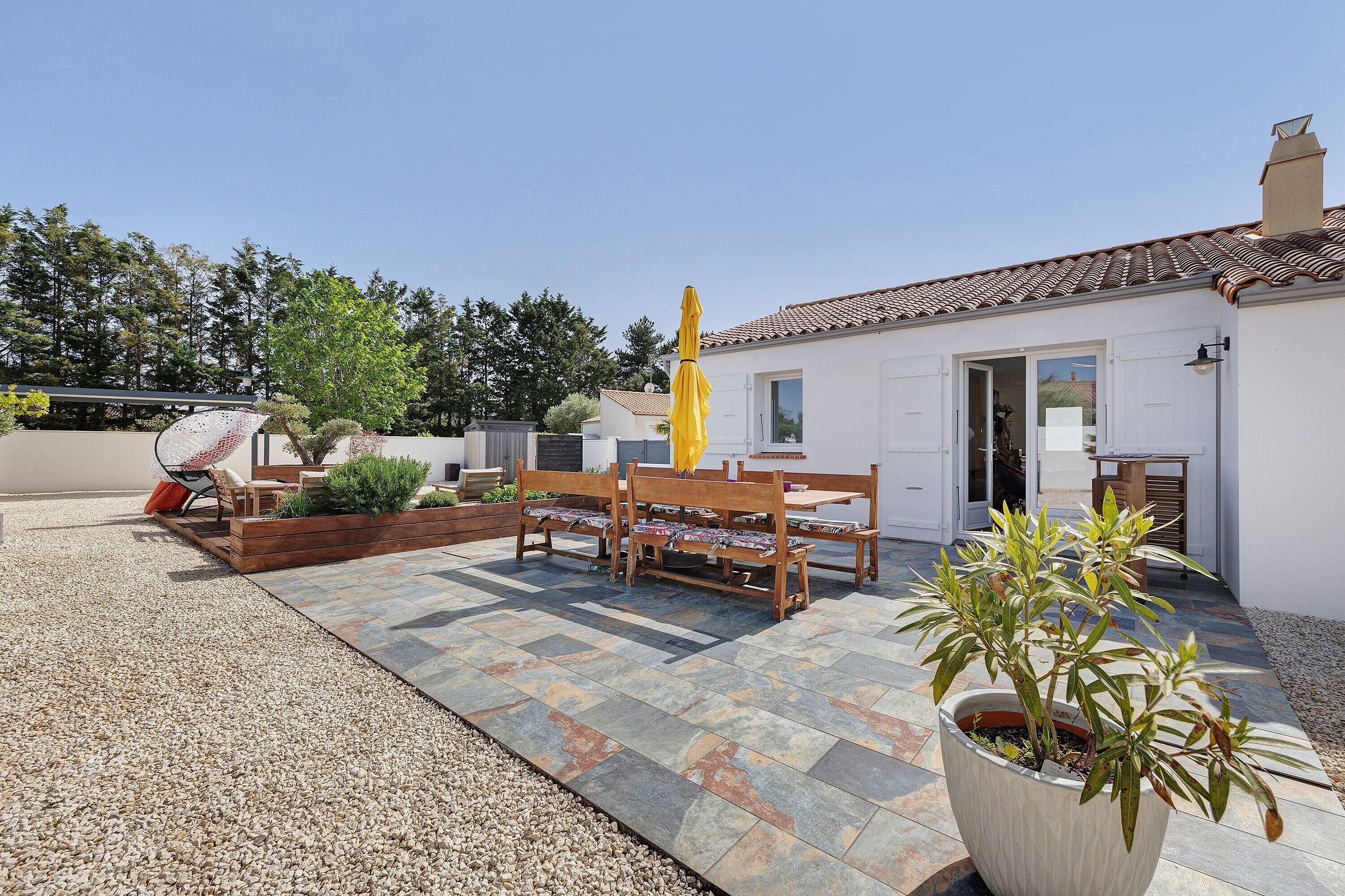 A patio with a bench, a potted plant, and a yellow umbrella.