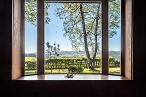 Ein Zimmer mit großem Fenster und Blick auf eine grüne Landschaft mit Bäumen und einem Zaun.