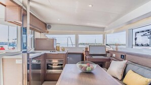Eine kleine Kombüse mit Esstisch, einer Sitzecke mit Kissen und Blick auf den Hafen.