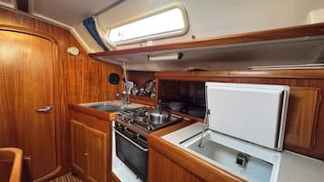 A compact kitchen with wooden cabinets, a stove, a sink, and a refrigerator.