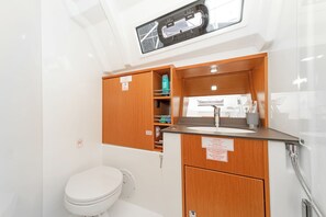 Ein kleines Badezimmer mit Toilette, Holzschränken, einem Waschbecken und einer Dusche.