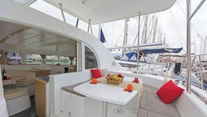 A yacht interior with a dining area, a small kitchen, and a seating area with cushions. - Sun-Kissed Sailing Adventure in Islas Sarónicas (Alimos)