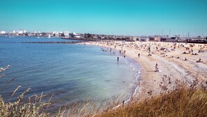 A beach with people, a pier, and buildings in the background. - Sun-Kissed Sailing Adventure in Antiguo Puerto de La Rochelle (La Rochelle)