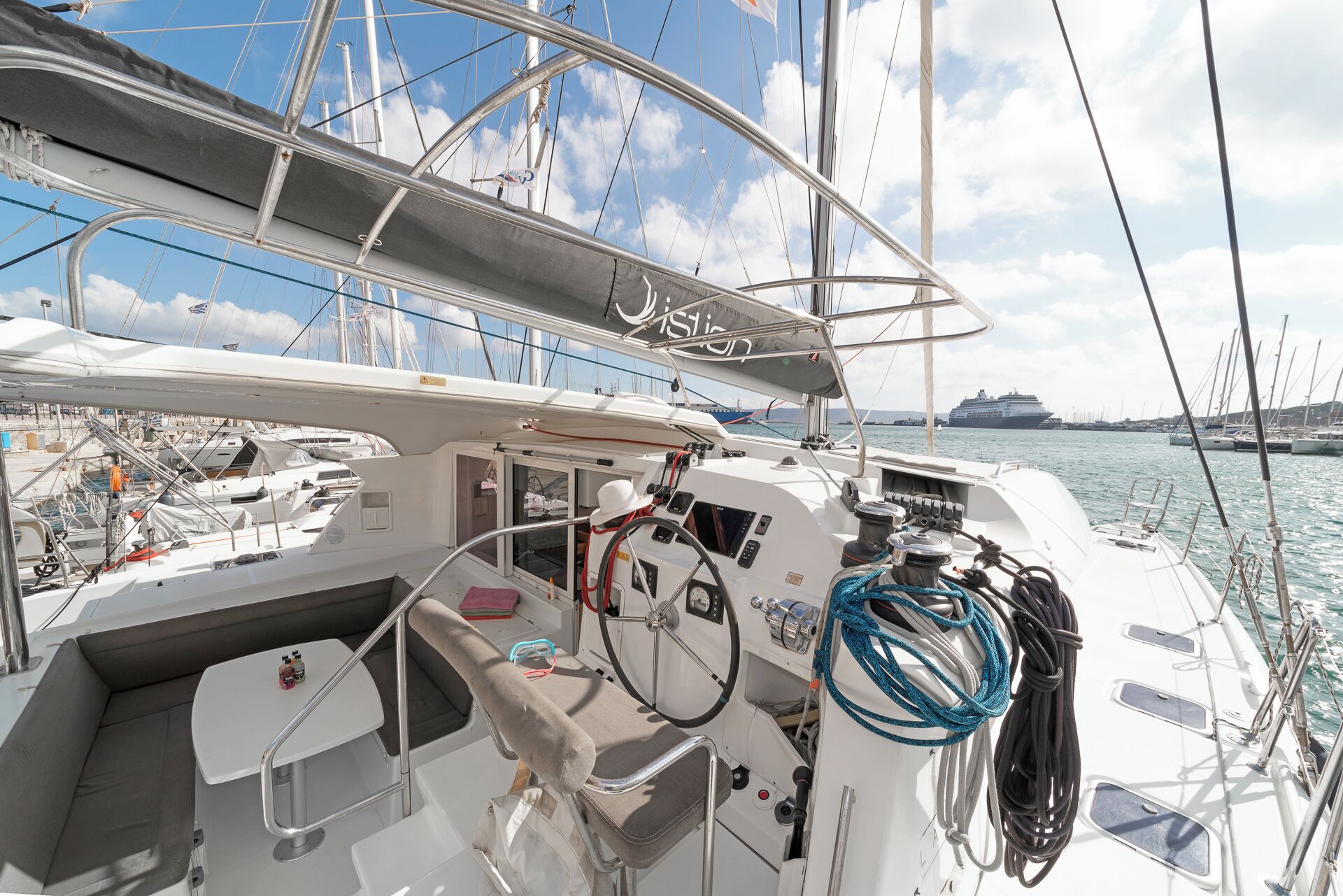 A sailboat's deck with a steering wheel, control panel, and coiled ropes.