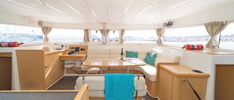 L'intérieur d'un yacht comprenant un coin repas, des sièges et une vue sur le port de plaisance.