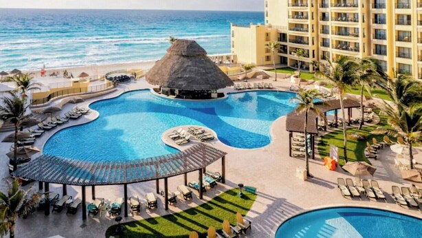 Een resort met een groot zwembad, ligbedden, een rieten constructie en uitzicht op de oceaan.
