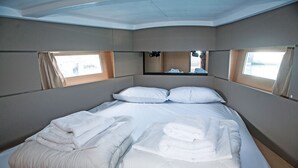 A neatly made bed with pillows and towels, a small mirror above it, and windows on either side. - Sun-Kissed Sailing Adventure in the Ionian Islands, Lefkada (Lefkada)