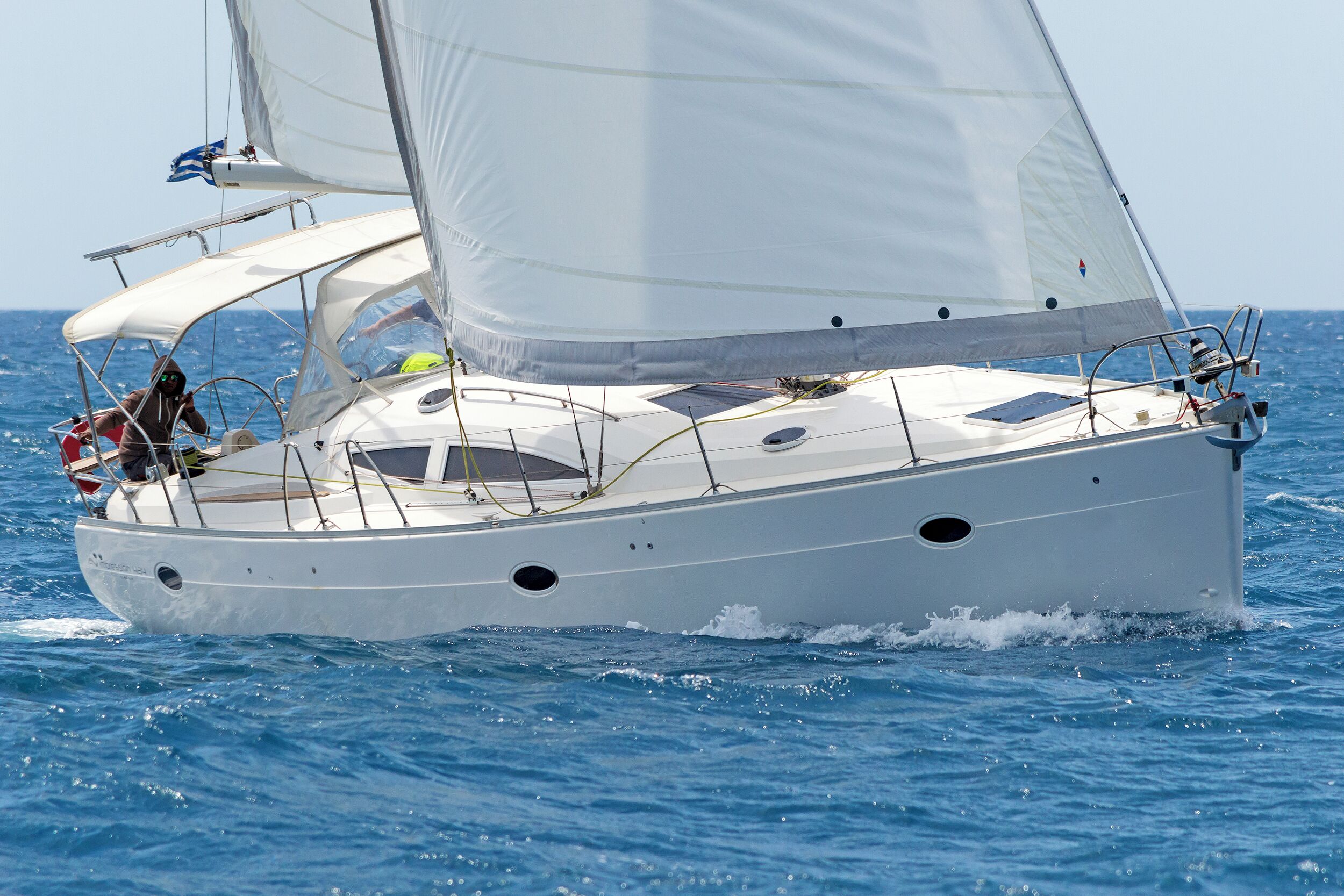 A sailboat with a cabin, a person at the helm, and a clear blue sky.