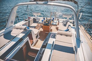 A boat's deck with a dining table, chairs, and a small seating area. - Sun-Kissed Sailing Adventure in Islas Sarónicas (Alimos)
