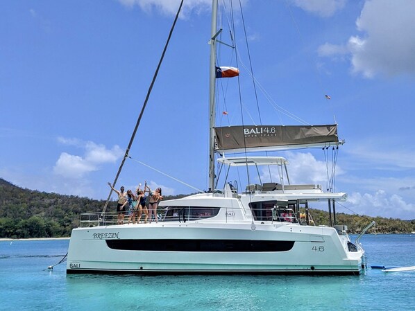 A white yacht named 'BALI 4.6' with a 'BALI' logo on the bow, docked in clear turquoise waters with a forested island in the background.