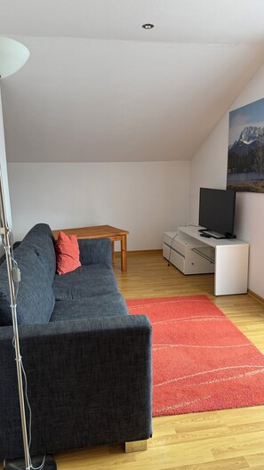 Ein modernes Wohnzimmer mit einem grauen Sofa, einem Holztisch, einem Fernseher auf einem weißen Schrank und einem roten Teppich.