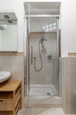 Une douche fermée par des parois en verre, dotée d’un pommeau de douche à main, d’un robinet mural et d’un drain au sol.