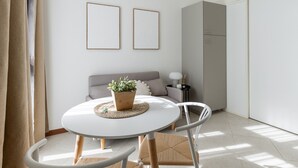 A modern living room with a round table, two framed pictures on the wall, a grey sofa, and a grey cabinet. - Light-Filled Flat by Wonderful Italy (Bologna)