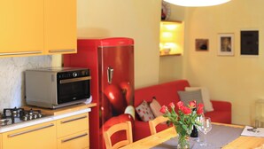 Een compacte keuken met een rode koelkast, een magnetron en een gasfornuis. Er staat een eettafel met een bloevas en twee wijnglazen.
