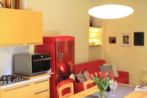 A compact kitchen with a red refrigerator, a microwave, and a gas stove. There is a dining table with a vase of flowers and two glasses. - Charming Apartment in Historic Lucca With Modern Comforts (Lucca)
