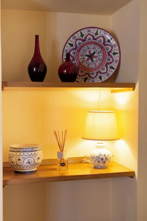 A shelf with decorative items including a plate, two vases, a lamp, and a small bottle. - Charming Apartment in Historic Lucca With Modern Comforts (Lucca)