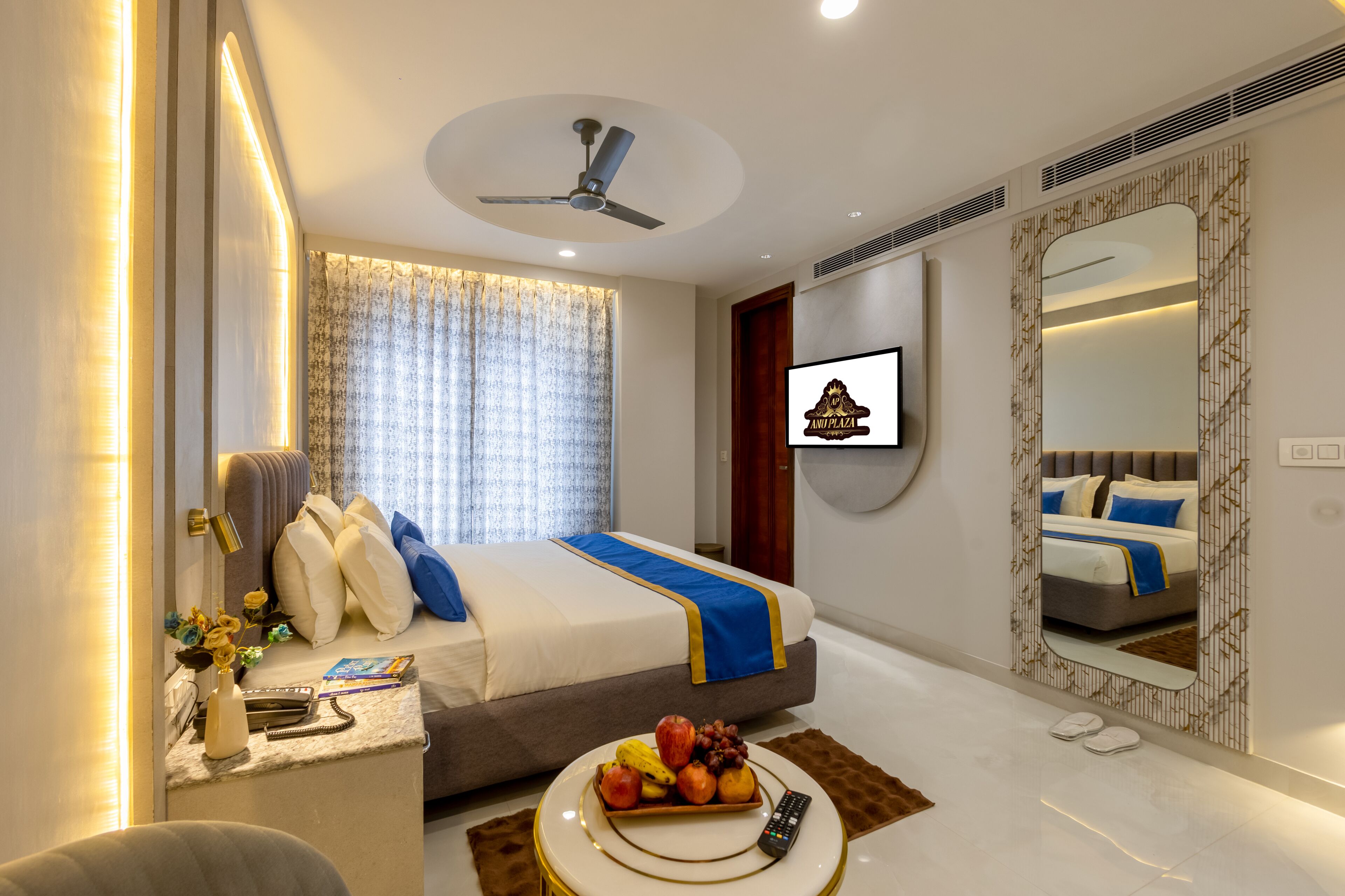 A modern hotel room with a bed, bedside table, fruit bowl, remote control, and a television.