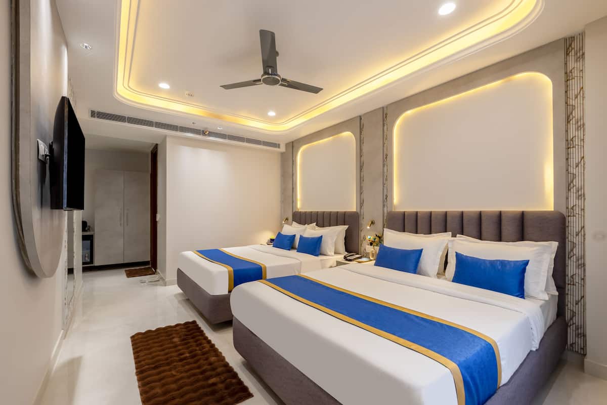 A modern hotel room with two beds, a ceiling fan, recessed lighting, and a flat-screen TV.
