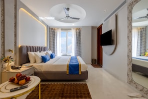 Una habitación de hotel moderna con cama, televisión de pantalla plana, ventilador de techo y un espejo grande.