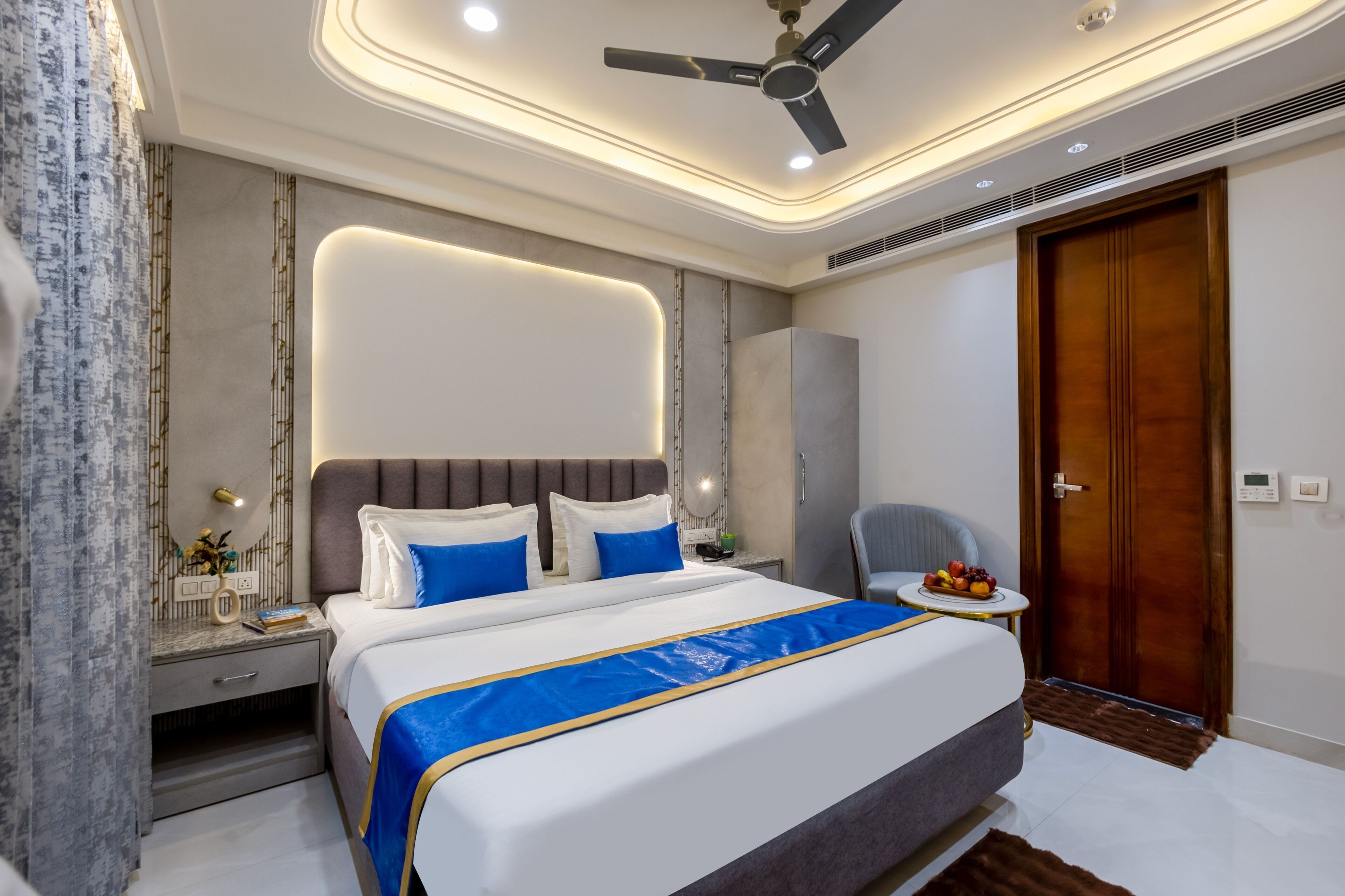 Une chambre d’hôtel moderne avec un grand lit, une table de chevet et une petite table sur laquelle sont disposés des fruits.