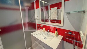 Un bagno con box doccia in vetro, un lavandino bianco, uno specchio e pareti rivestite di piastrelle bianche e rosse.