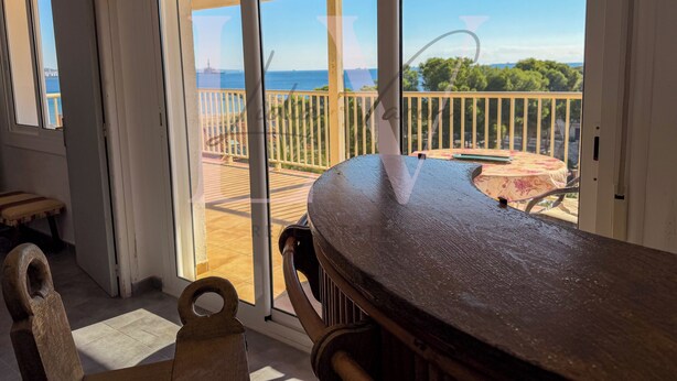 Una stanza con un tavolo di legno, una sedia e una porta scorrevole in vetro che dà su una terrazza esterna con vista sul mare.