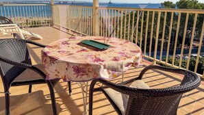 Un balcone con tavolo e sedie, affacciato su un tratto d'acqua e la costa in lontananza.