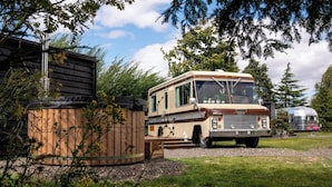 A camper van parked in a grassy area with a wooden structure and a metal grill in the foreground. - Sleeps 2 -pets Welcome -private Hot Tub -alabama (Skegness)