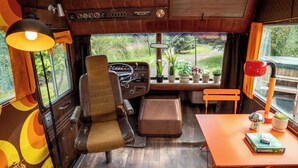 A cozy interior with a wooden dashboard, a steering wheel, a small table with a Scrabble game, and a window with a view of greenery. - Sleeps 2 -pets Welcome -private Hot Tub -alabama (Skegness)
