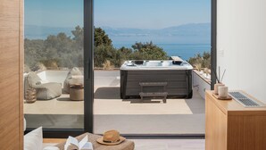 Habitació moderna amb una gran porta corredissa de vidre que dona a una zona exterior amb mobiliari d'estil, una banyera d'hidromassatge i vista al mar.